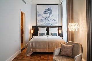 Elegantes Schlafzimmer mit Doppelbett, Kunstwerk, gemütlichem Sessel und stilvoller Beleuchtung.