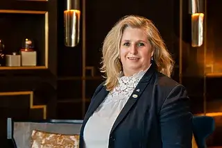 Professionelle Frau in eleganter Kleidung, lächelnd vor modernem Hintergrund.